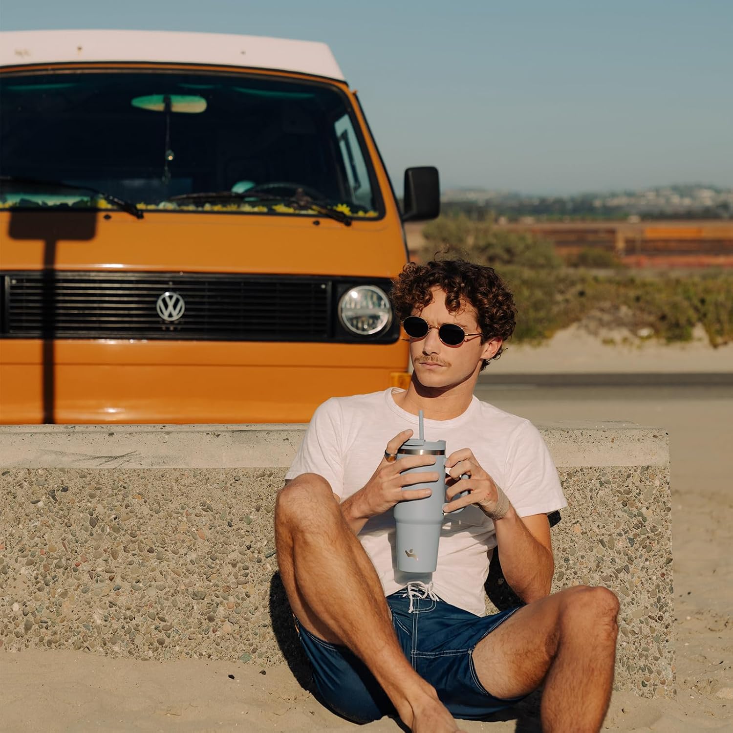Man sitting in front of a yellow Volkswagen van holding a tumbler.