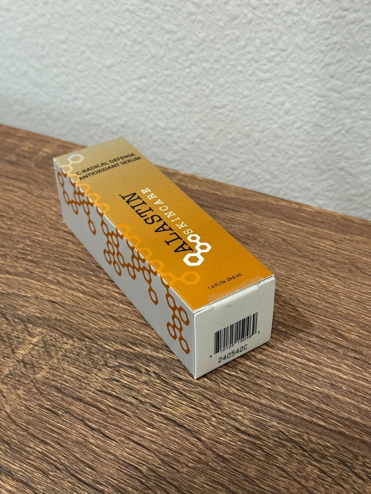 A box of ALASTIN Collagen Defense Antioxidant Serum placed diagonally on a brown wooden tabletop against a textured white wall.