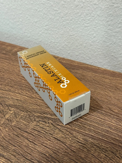 A box of ALASTIN Collagen Defense Antioxidant Serum placed diagonally on a brown wooden tabletop against a textured white wall.