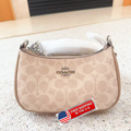 A Coach shoulder bag in beige signature canvas with silver-tone hardware, resting on a light textured surface. A red and white 'FREE SHIPPING IN THE U.