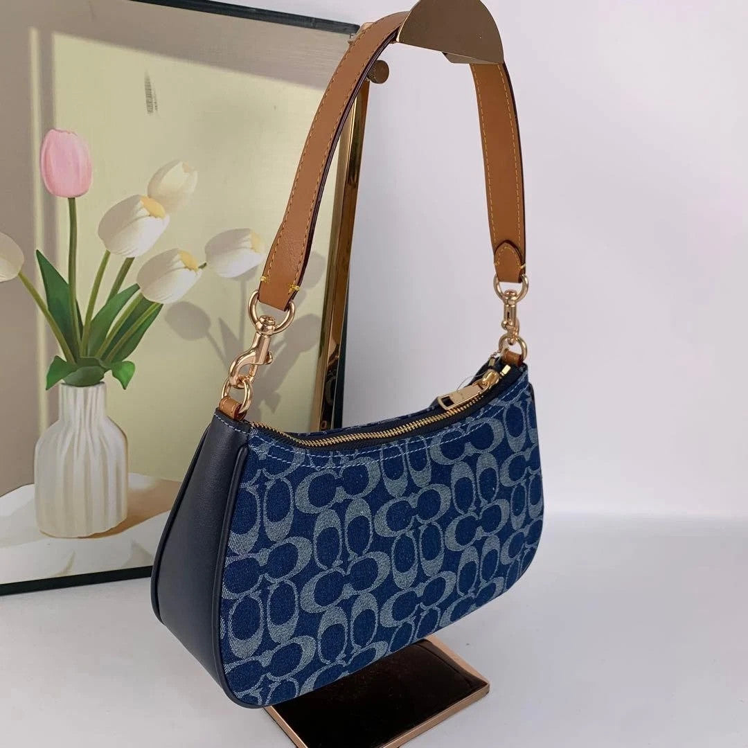 A blue leopard-print shoulder bag with brown leather handles, displayed on a stand in front of a picture frame.