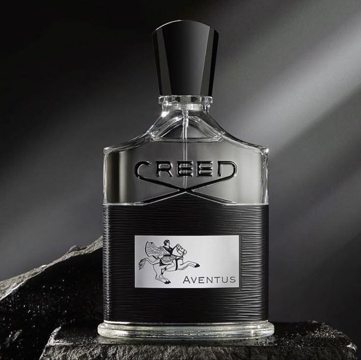 Creed Aventus perfume bottle with a black cap and a black-and-silver textured body, displayed on a dark stone surface against a dramatic dark gray background.