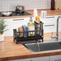 Black dish rack with kitchen items on a wooden countertop next to a sink.