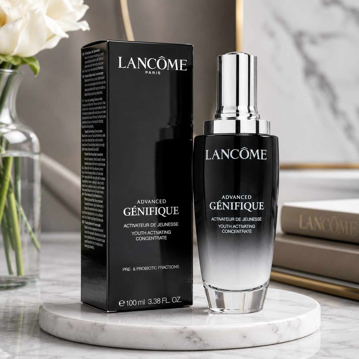 Lancôme Advanced Génifique youth activating concentrate shown as a black gradient bottle with a silver cap next to its black packaging box, set on a marble tray with a marble background and white roses.