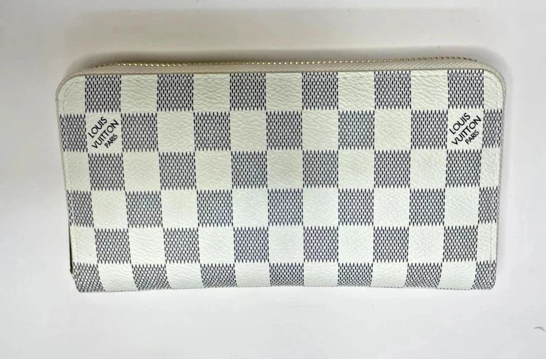 Louis Vuitton zip-around wallet in the Damier Azur checkerboard pattern, featuring alternating white and light gray textured squares with black brand logos on the sides.