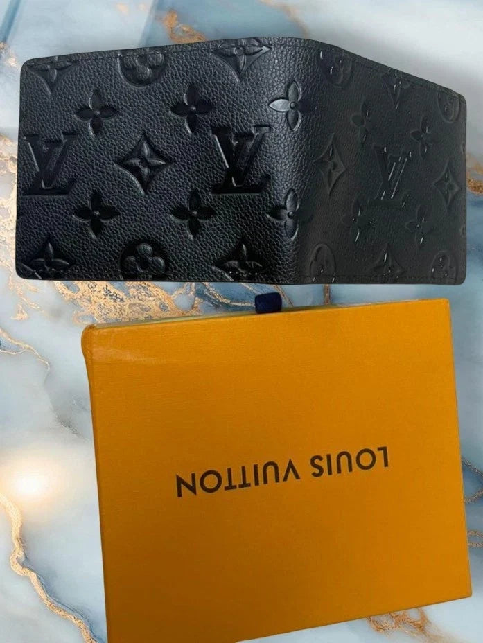 A black Louis Vuitton monogram embossed leather wallet shown above its signature orange box on a light marble surface.