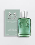Greenley cologne bottle and its matching box by Parfums de Marly, featuring a translucent green glass bottle with an embossed horse crest and a silver cap, next to a sage green box with silver horse illustrations.