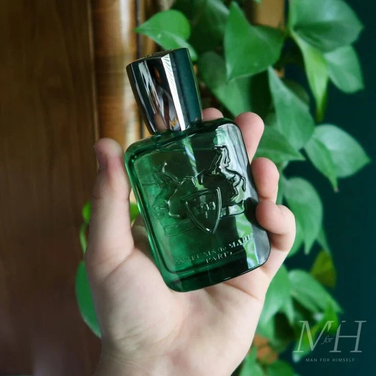 Hand holding a green perfume bottle with a blurred plant background
