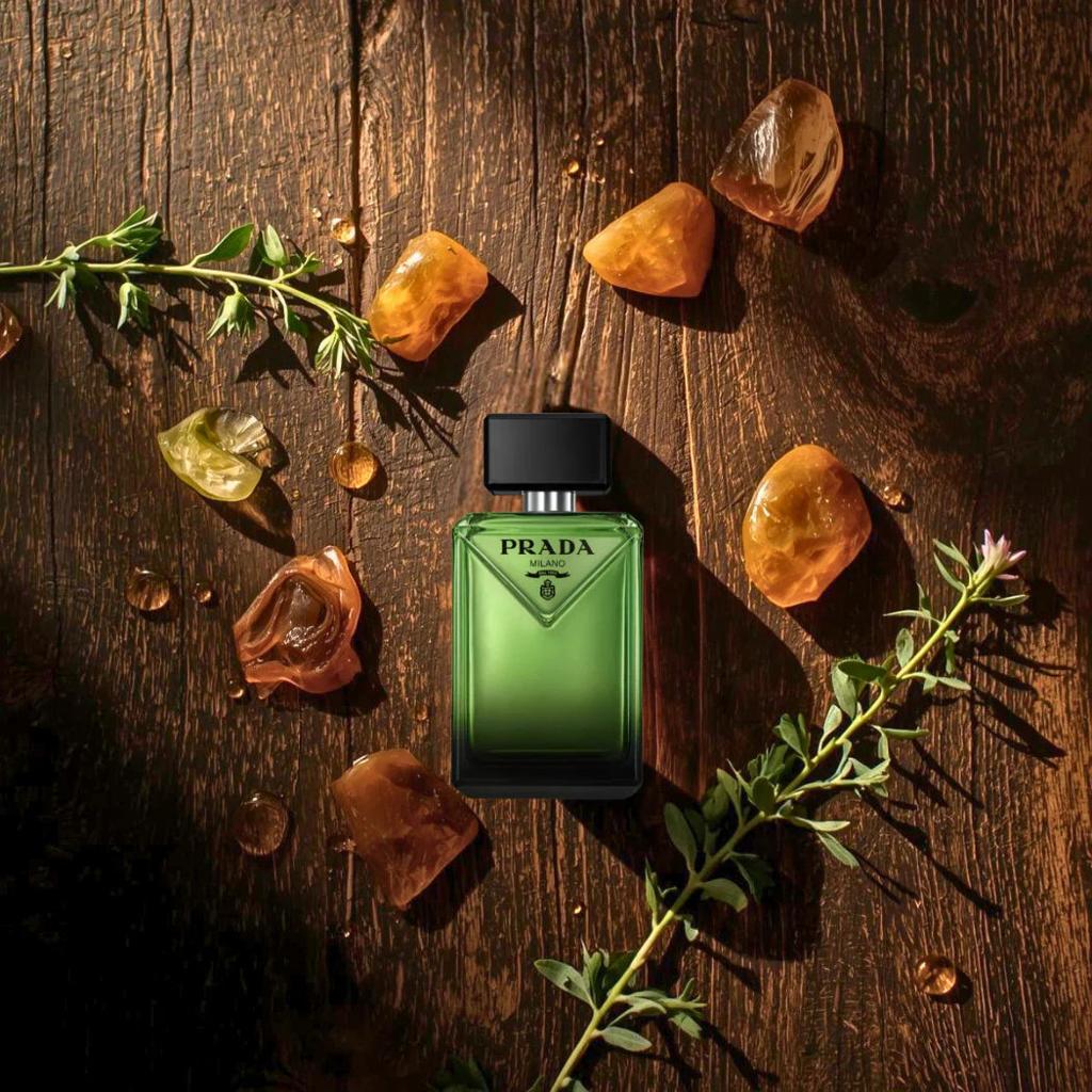 Green Prada perfume bottle on a wooden surface with amber stones and green leaves.