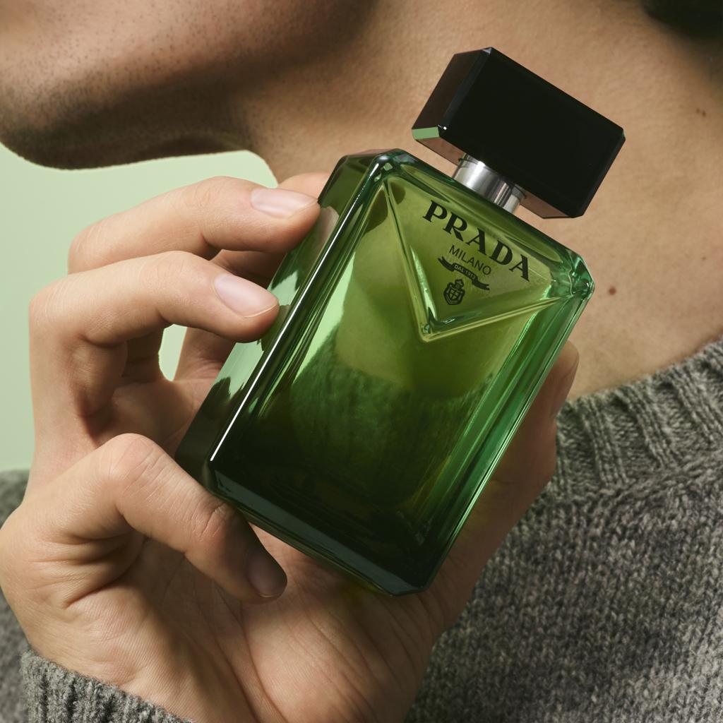 Green Prada perfume bottle held by a hand against a neutral background