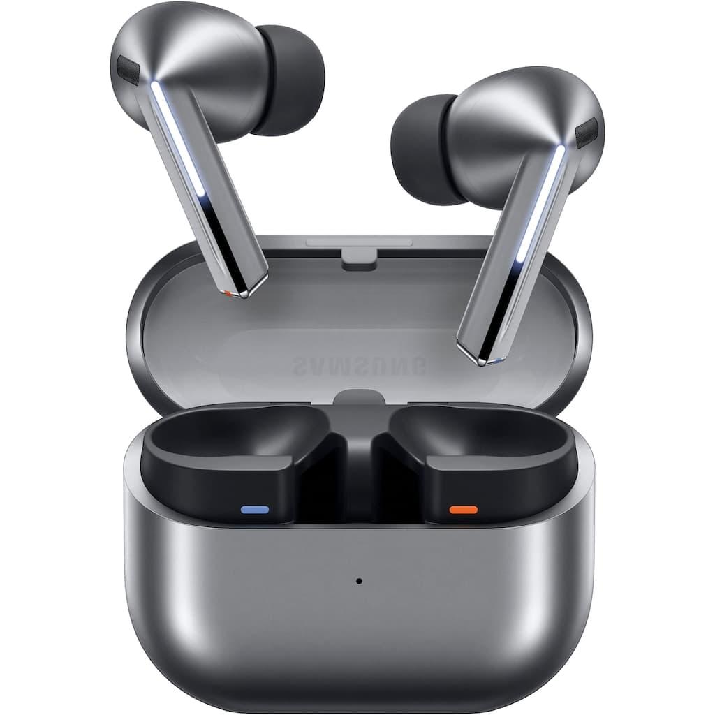 True wireless earbuds in a metallic dark gray charging case, shown open with both earbuds positioned above the compartment. The earbuds have black tips and a brushed silver finish, with small blue and orange indicator lights visible inside the case.