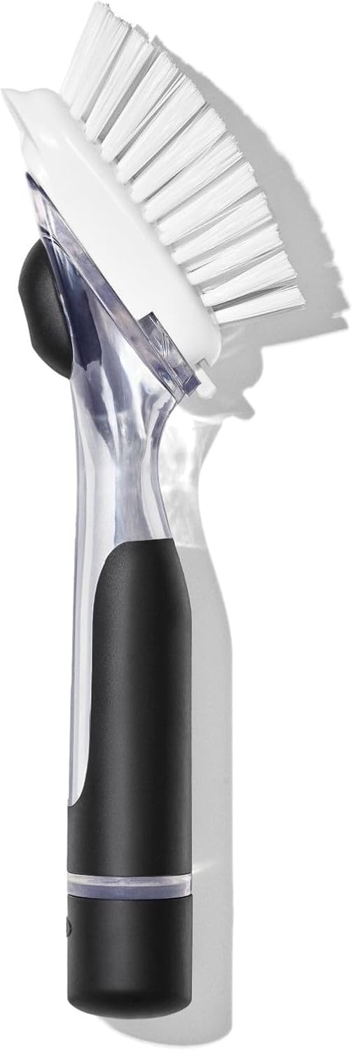 A dual-sided electric cleaning brush with a black handle, clear plastic body, white bristles, and a black rubber scrubber pad, shown on a white background with a soft shadow.