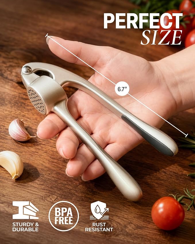 A hand holding a garlic press over a wooden surface with garlic cloves and tomatoes around it. White text reads 'PERFECT SIZE' with a measurement line showing 6.