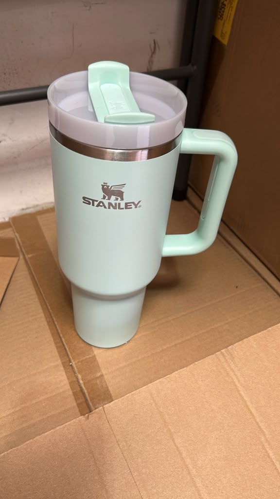 A mint green Stanley travel tumbler with a matching lid and handle, resting on a cardboard box.