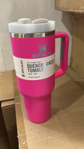 A bright pink Stanley Quencher H2O travel tumbler with a white lid and handle, resting on a cardboard box.