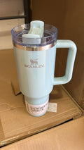 A light blue Stanley Quencher 32 oz handled tumbler with a clear lid and white flip-top spout, resting on a cardboard box.