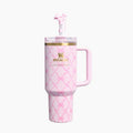 A pink Stanley tumbler with a matching pink handle and straw, decorated with a pink bow pattern and a gold logo on the front, set against a plain white background.