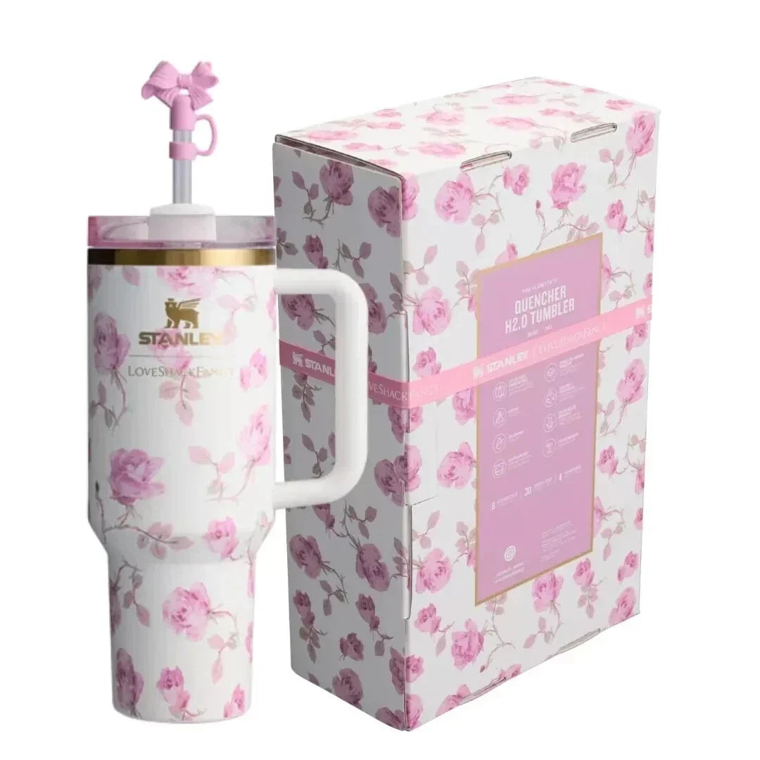 A pink and white floral patterned stainless steel travel mug with a handle and straw, shown next to its matching retail box. The packaging features a matching floral design with a pink label.