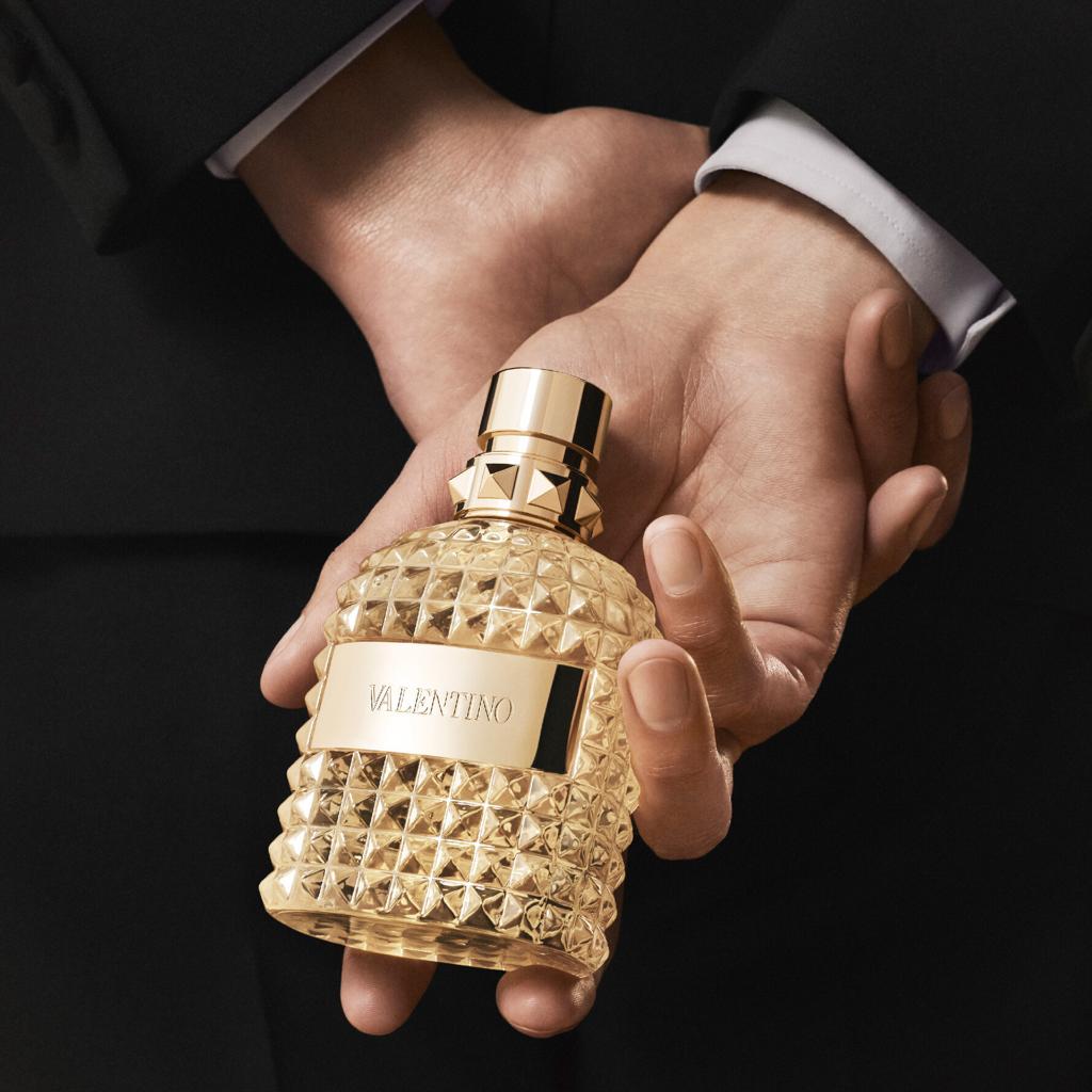 Gold perfume bottle held by a hand with a dark background