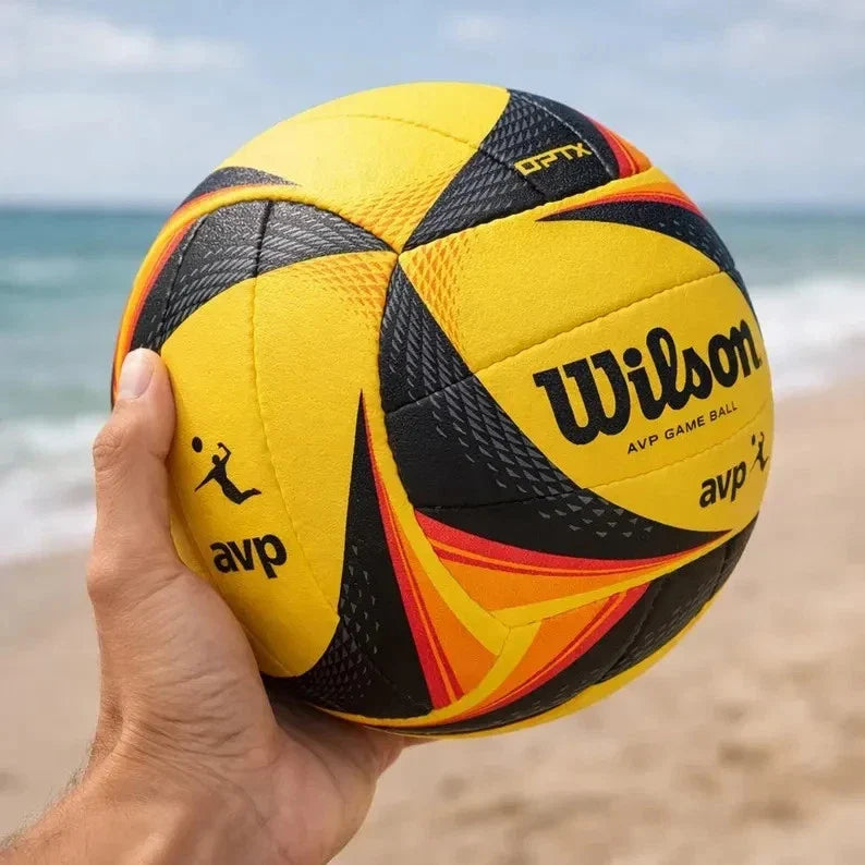 Yellow and black Wilson volleyball held by a hand on a beach.